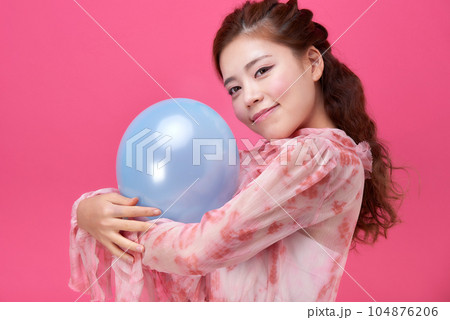 female model wearing a flower-patterned dress with a pink background and blowing blue balloons 104876206