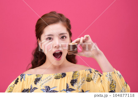 female model wearing a flower-patterned dress with a pink background and enjoying snacks female model wearing a flower-patterned dress with a pink background and enjoying snacks 104877118