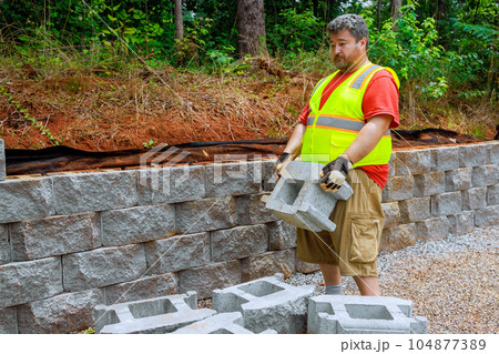 It was responsibility of construction worker to lift concrete block and place it on retaining wall. It was responsibility of construction worker to lift concrete block and place it on retaining wall. 104877389