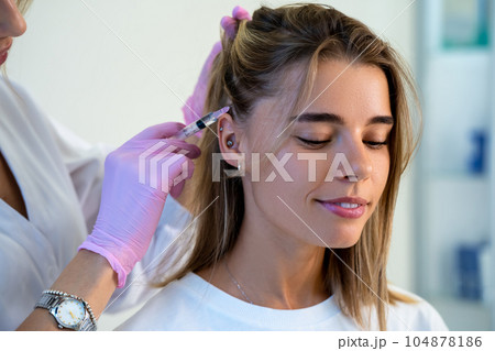 Unrecognizable doctor doing vitamin injections in customers head skin of hair area. 104878186
