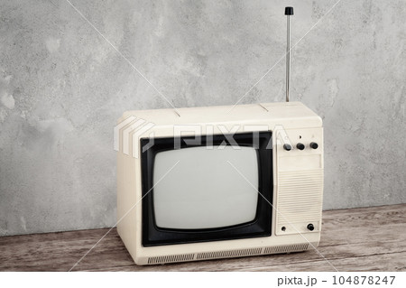 Vintage analog small TV set stand on wooden floor front grey concrete wall. 104878247