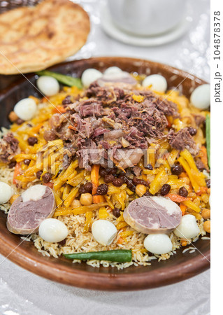 Rice with meat, carrots, onions, quail eggs and kazy in a plate of astau on the table. A traditional Uzbek dish called pilaf. A portion for three people. Rice with meat, carrots, onions, quail eggs and kazy in a plate of astau on the table. A traditional Uzbek dish called pilaf. A portion for three people. 104878378