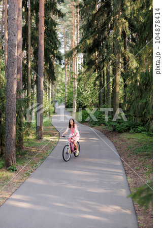 young active woman in pink dress rides a bicycle in park among the trees 104878414