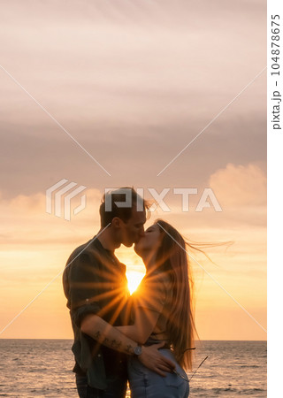 silhouettes in love romantic couple lovers hugging, kissing, touching, eye contact at sunset, sunrise on the background of the sea, the sun, the clouds in fiery red, orange colors 104878675