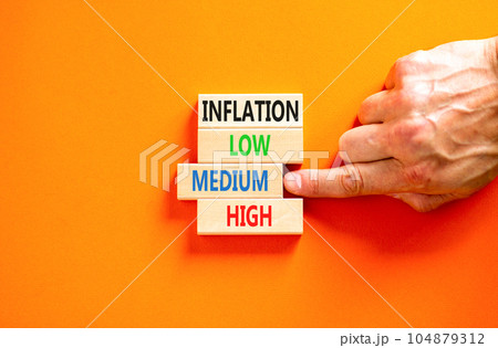 Medium inflation symbol. Concept word Inflation low medium high on wooden block. Businessman hand. Beautiful orange table orange background. Business time to medium inflation concept. Copy space. 104879312