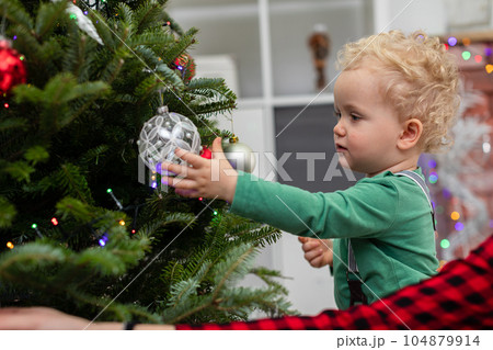 A little boy plays with a bauble hung on a Christmas tree. A little boy plays with a bauble hung on a Christmas tree. 104879914