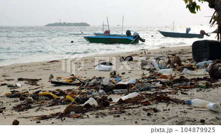 Lots of trash on sandy coast by the fishing boats and ocean waves. Environmental pollution concept 104879925