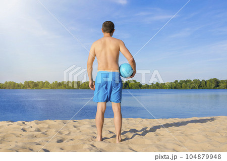 A man with a volleyball ball on the beach on a sunny day. The view from the back A man with a volleyball ball on the beach on a sunny day. The view from the back 104879948