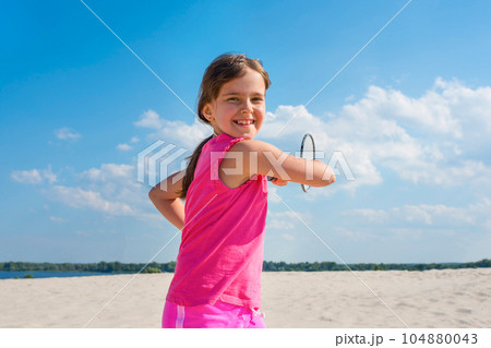 Outdoor portrait of happy girl playing beach badminton on the beach. 104880043