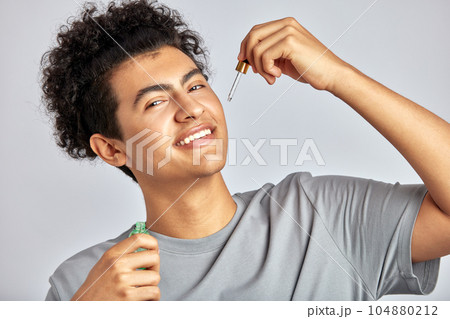 Happy young smiling guy applying beauty serum on his face. Swarthy man with black curly hair uses beauty products maintaining his natural beauty with skincare routine. Men's self-care. Happy young smiling guy applying beauty serum on his face. Swarthy man with black curly hair uses beauty products maintaining his natural beauty with skincare routine. Men's self-care. 104880212