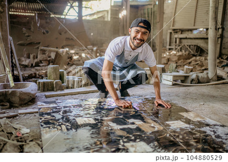 Smiling stonemason squats while washing large squares of stone 104880529