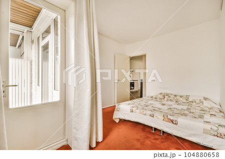 a bedroom with red carpet and white walls, there is a small bed in the room next to the window 104880658
