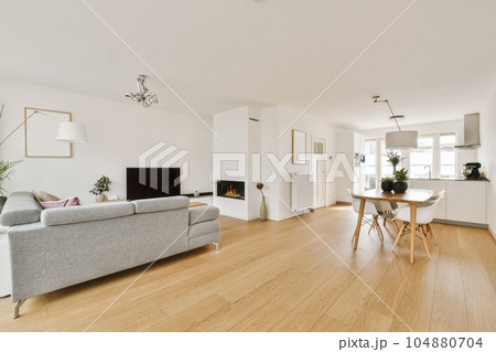 a living room with white walls and wood flooring in the center of the room, there is a grey couch a living room with white walls and wood flooring in the center of the room, there is a grey couch 104880704