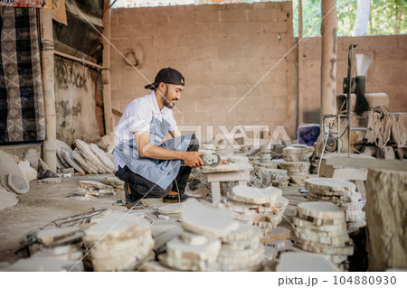 side view of a stone craft worker squatting while cutting stones 104880930