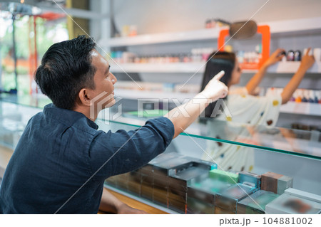 male customer pointing on the liquid arranged at the store shelf 104881002