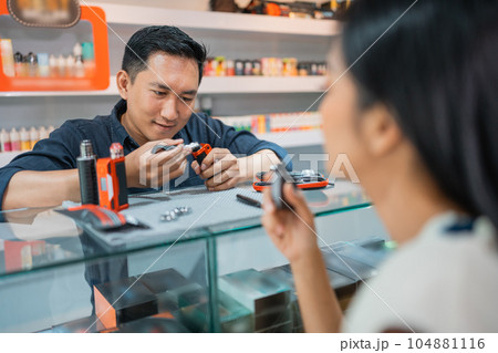 male shopkeeper changing the vape cotton in front of the vaping woman 104881116