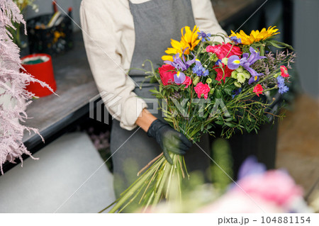 Close up of woman flower shop owner in apron holding bouquet of flowers at florist store Close up of woman flower shop owner in apron holding bouquet of flowers at florist store 104881154