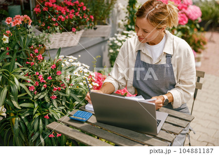 Professional flower shop owner florist using laptop and writing on notebook at flower shop Professional flower shop owner florist using laptop and writing on notebook at flower shop 104881187