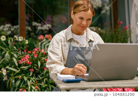 Professional flower shop owner florist using laptop and writing on notebook at flower shop 104881200