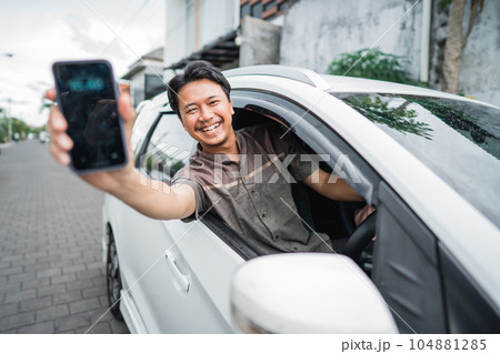 male driver showing his mobile phone screen while sitting in a car male driver showing his mobile phone screen while sitting in a car 104881285