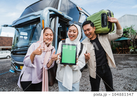 traveler with suitcase showing blank screen standing in front of bus 104881347