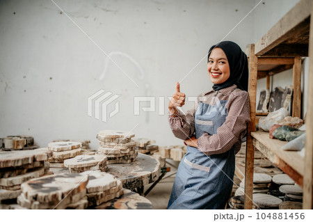 Muslim woman smiling with thumbs up leaning on a shelf 104881456