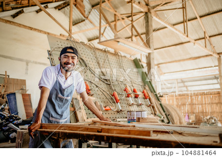 Asian entrepreneur in a hat smiling in a woodcraft workshop 104881464