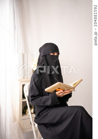 muslim woman wearing black hijab long dress is sitting reading al qur'an 104881592