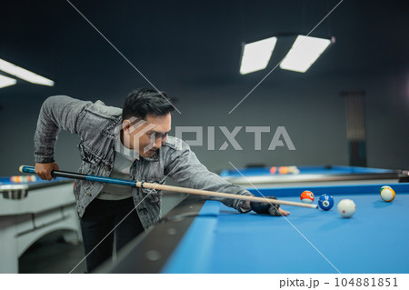 male billiard player poking the ball seriously using the cue stick male billiard player poking the ball seriously using the cue stick 104881851