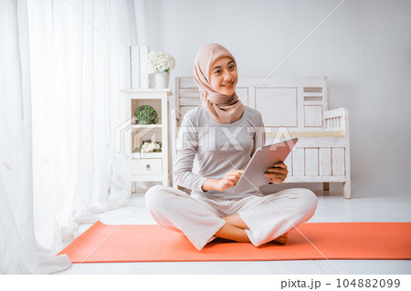 Muslim hijab woman watching exercise home workout tutorial from tablet in room Muslim hijab woman watching exercise home workout tutorial from tablet in room 104882099
