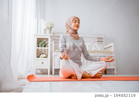 healthy muslim woman wearing hijab doing yoga pilates meditating on mattress 104882119