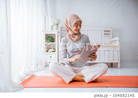 Muslim hijab woman watching exercise home workout tutorial from tablet in room Muslim hijab woman watching exercise home workout tutorial from tablet in room 104882148