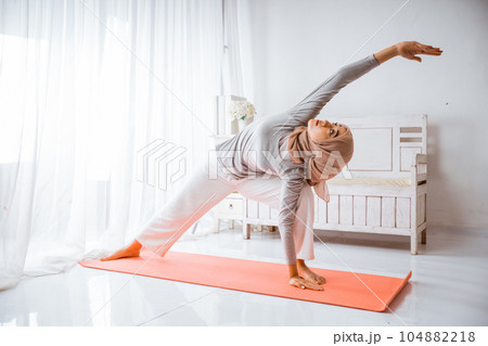 muslim woman instructor wearing hijab doing yoga pilates pose on mattress 104882218