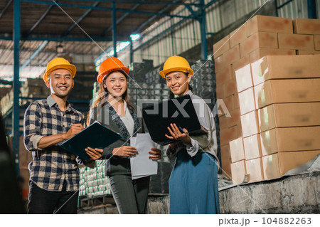 three smiling company employees standing using a laptop inside the factory 104882263
