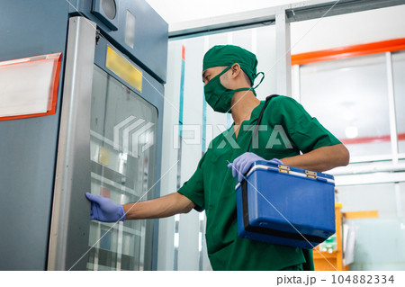 man in sterile clothes and mask carrying a blood bag box man in sterile clothes and mask carrying a blood bag box 104882334