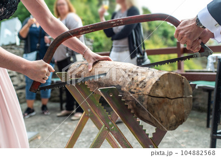 Young bridal couple groom bride sawing a tree trunk together german wedding tradition 104882568