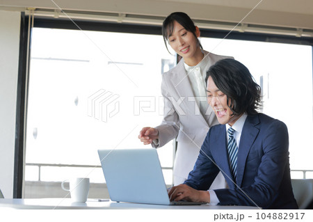 気合を入れて資料作成に打ち込むビジネスマンと近寄る同僚の女性_1 104882917