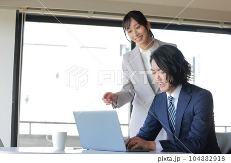 気合を入れて資料作成に打ち込むビジネスマンと近寄る同僚の女性_2 気合を入れて資料作成に打ち込むビジネスマンと近寄る同僚の女性_2 104882918