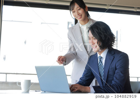 にこやかに資料作成に打ち込むビジネスマンと資料を確認する同僚の女性_1 104882919