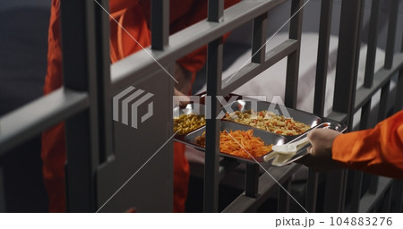 Prison guard gives food to prisoner through metal bars 104883276