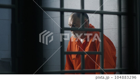 Criminal in orange uniform sits on prison bed Criminal in orange uniform sits on prison bed 104883296