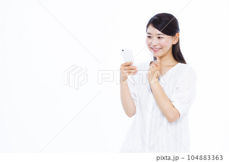 白い背景の前でスマホを持ち悩んでいる30代の女性 104883363