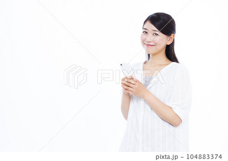 白い背景の前で笑顔でスマホを持っている30代の女性 104883374