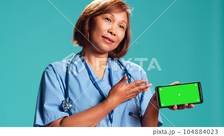 Close up shot of clinic employee isolated over studio background showing medical tape on chroma key phone green screen. Nurse holding smartphone in landscape mode, presenting informative video Close up shot of clinic employee isolated over studio background showing medical tape on chroma key phone green screen. Nurse holding smartphone in landscape mode, presenting informative video 104884023