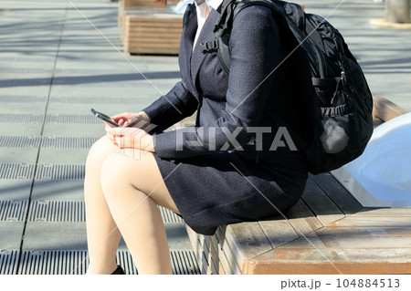 リュックを背負ってベンチに座っているビジネスウーマン リュックを背負ってベンチに座っているビジネスウーマン 104884513