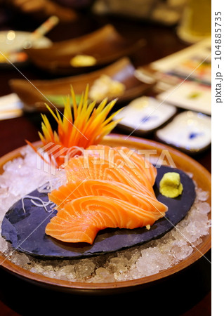 Close-up shallow focus of salmon sashimi beautifully arranged on a stone slab. There was wasabi next to it. and flower ornaments on ice mounds in round bowls. Beautifully arranged, blurred background. Close-up shallow focus of salmon sashimi beautifully arranged on a stone slab. There was wasabi next to it. and flower ornaments on ice mounds in round bowls. Beautifully arranged, blurred background. 104885735