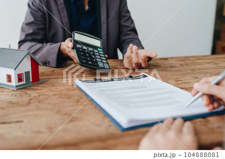 Guarantee, mortgage, contract, contract, signed, real estate agent or bank officer holding a calculator, submits a bid with a customer to buy a home before signing to make a deal. 104888081