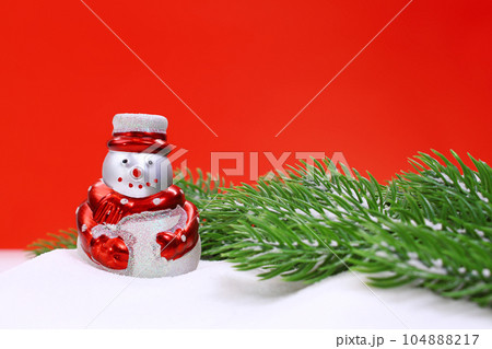 Snowman in the snow and green spruce branches on red background. Christmas, New Year. Copy space 104888217