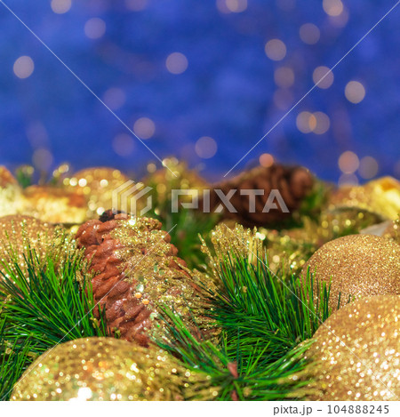 Shiny yellow Christmas balls and cone with barks and pine branches. Blue background with bokeh. New year card. Copy space 104888245