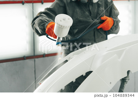 Male painter in respiratory mask and protective suit painting car with spray gun in car service 104889344